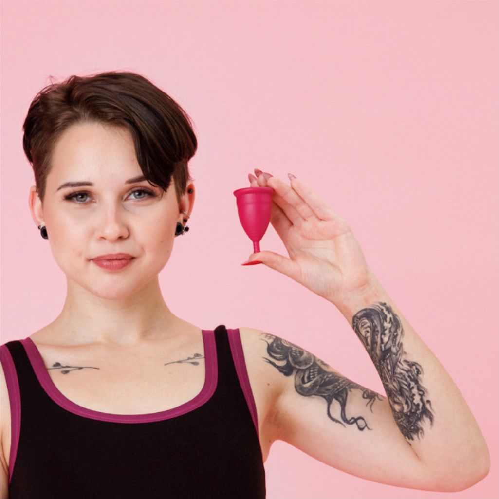 Moteris rankoje laiko GENIAL DAY menstruacinę taurelę prieš rožinį foną